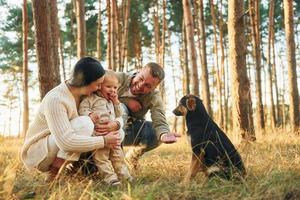 jugando con perro. feliz familia de padre, madre e hija pequeña está en el bosque foto