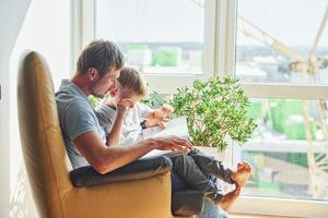 Sitting with book. Beautiful sunlight. Father and son is indoors at home together photo