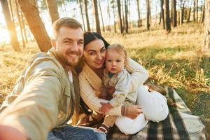Making a selfie. Happy family of father, mother and little daughter is in the forest photo