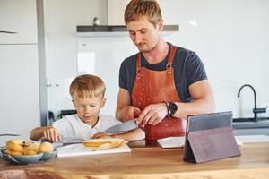 en la cocina con comida. padre e hijo están juntos en casa en el interior foto