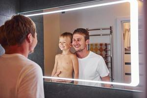 Looking in the mirror in bathroom. Father and son is indoors at home together photo