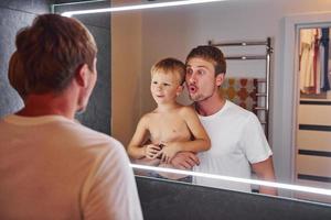 Looking in the mirror in bathroom. Father and son is indoors at home together photo