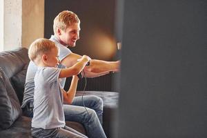 sosteniendo controladores de videojuegos. padre e hijo están juntos en casa en el interior foto