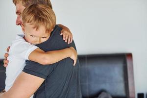 abrazándose unos a otros. padre e hijo están juntos en casa en el interior foto