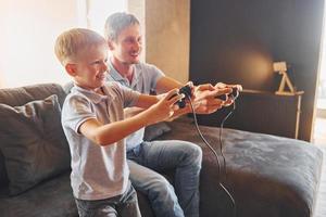 con joysticks de videojuegos. padre e hijo están juntos en casa en el interior foto