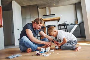 Sitting on the floor and playing with toys. Father and son is indoors at home together photo