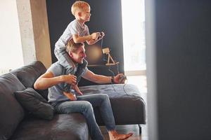 niño está sentado sobre los hombros del hombre. padre e hijo están juntos en casa en el interior foto