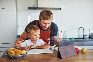 aprendiendo a cocinar. padre e hijo están juntos en casa en el interior foto