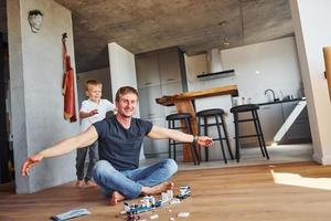 sentado en el suelo y jugando con juguetes. padre e hijo están juntos en casa en el interior foto