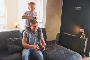 Playing video game. Father and son is indoors at home together photo
