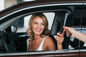 Holding car keys. Woman in formal clothes is indoors in the autosalon photo