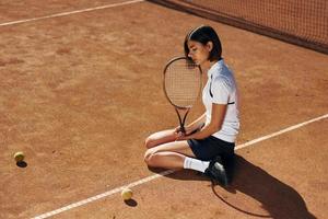 On the ground. Female tennis player is on the court at daytime photo