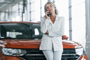 Using phone. Woman in formal clothes is indoors in the autosalon photo