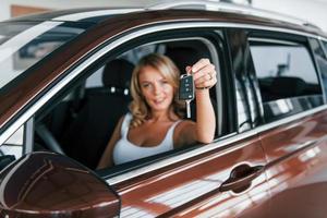 Holding car keys. Woman in formal clothes is indoors in the autosalon photo