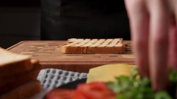 Woman preparing sandwich with ham and cheese slice in the kitchen, closeup video