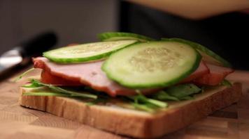 Woman preparing sandwich with ham and cheese slice in the kitchen, closeup video