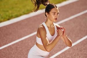 Doing squats. Young woman in sportive clothes is exercising outdoors photo