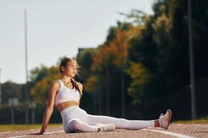 Sitting on the ground. Young woman in sportive clothes is exercising outdoors photo