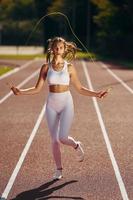 Practicing with jumping rope. Young woman in sportive clothes is exercising outdoors photo