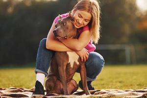 Lying down on a blanket. Woman in casual clothes is with pit bull outdoors photo