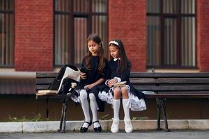 Two schoolgirls is sitting outside together near school building photo