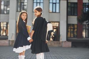 Caminando juntos. dos colegialas están afuera cerca del edificio de la escuela foto