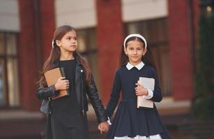 Walking together. Two schoolgirls is outside near school building photo