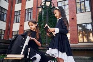 sentados juntos. dos colegialas están afuera cerca del edificio de la escuela foto