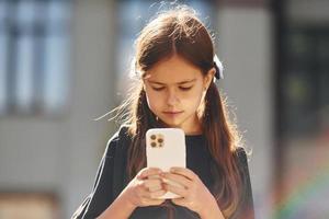 With smartphone in hands. Schoolgirl is outside near school building photo