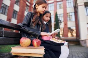 Sitting and reading. Two schoolgirls is outside together near school building photo