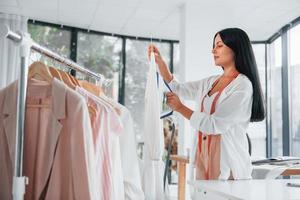 Irons clothes. Seamstress is in her office that is with different clothes photo