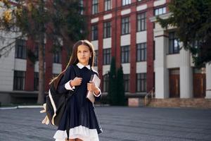 After lessons. Schoolgirl is outside near school building photo
