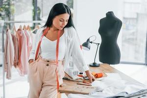 Standing by the table. Seamstress is in her office that is with different clothes photo