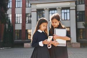 Front view. Two schoolgirls is outside together near school building photo