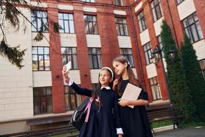 With books. Two schoolgirls is outside together near school building photo