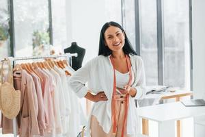 Standing and smiling. Seamstress is in her office that is with different clothes photo