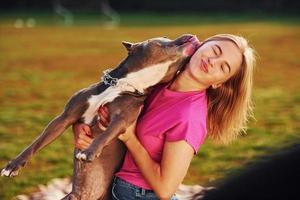 Positive emotions. Woman in casual clothes is with pit bull outdoors photo