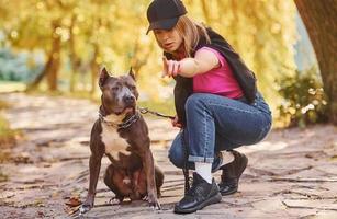 Yellow leaves at background. Woman in casual clothes is with pit bull outdoors photo