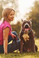 On the green grass. Woman in casual clothes is with pit bull outdoors photo