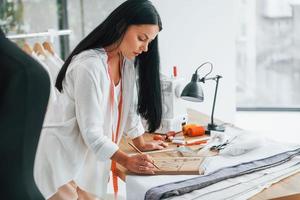 Working with precision. Seamstress is in her office that is with different clothes photo