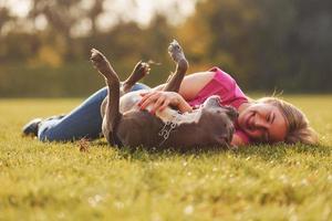 On the green grass. Woman in casual clothes is with pit bull outdoors photo