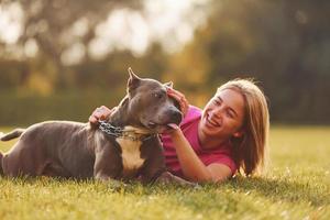 On the green grass. Woman in casual clothes is with pit bull outdoors photo