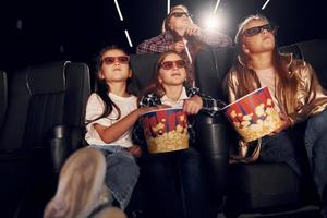 Front view. Group of kids sitting in cinema and watching movie together photo