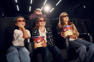 With popcorn. Group of kids sitting in cinema and watching movie together photo