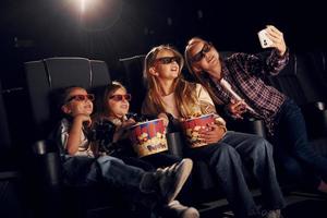 Making selfie. Group of kids sitting in cinema and watching movie together photo