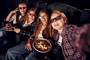 Making photo of each other. Group of kids sitting in cinema and watching movie together