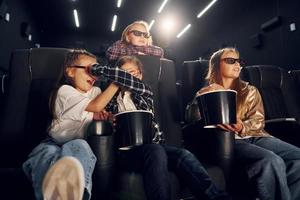 Eating popcorn. Group of kids sitting in cinema and watching movie together photo