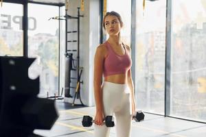 Standing with equipment. Beautiful young woman with slim body type is in the gym photo