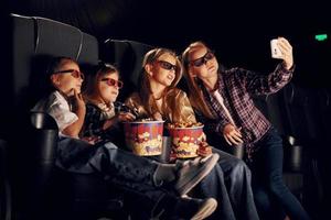 Making selfie. Group of kids sitting in cinema and watching movie together photo