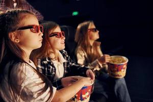 Eating popcorn. Group of kids sitting in cinema and watching movie together photo